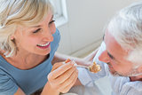 Close-up of a smiling woman feeding mature man pastry
