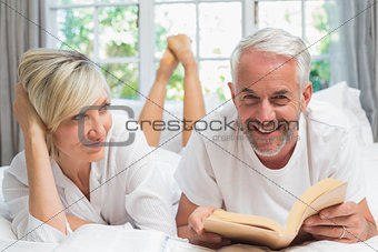 Happy mature couple reading book in bed