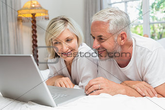 Happy mature couple using laptop in bed