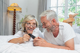 Cheerful mature couple reading text message at home