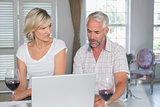 Mature couple with wine glasses using laptop