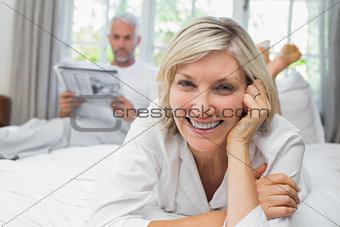 Smiling woman with man reading newspaper in bed