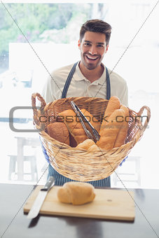 Happy young waiter with basket of breads at coffee shop counter