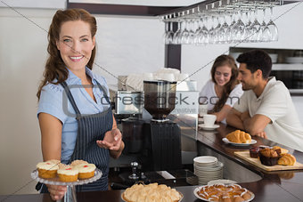 Smiling cafe owner holding sweet snacks with couple at counter in coffee shop