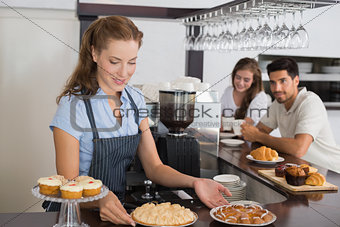 Cafe owner holding sweet snacks with couple at counter in coffee shop