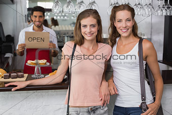 Female friends with male barista at counter in coffee shop