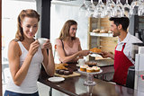 Woman drinking coffee with friend and barista in coffee shop