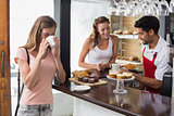 Woman drinking coffee with friend and male barista in coffee shop