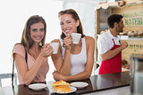 Smiling women drinking coffee with barista in background at coffee shop