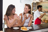 Women drinking coffee with barista in background at coffee shop