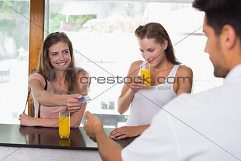 Women paying bill while drinking orange juice at coffee shop