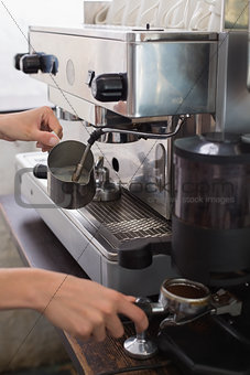Mid section of a barista prepares espresso in coffee shop