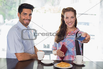 Couple with woman holding out credit card at coffee shop