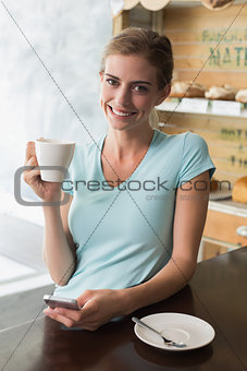 Woman drinking coffee while using mobile phone at counter in coffee shop