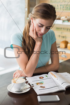 Concentrated woman with coffee cup reading magazine in coffee shop