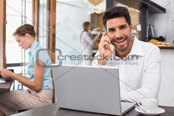 Happy man using laptop and mobile phone in coffee shop