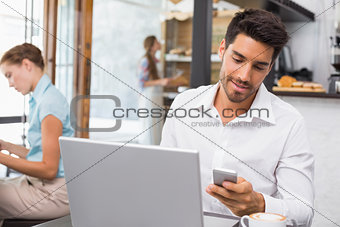 Man using laptop and mobile phone in coffee shop