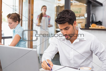 Man writing notes with laptop in coffee shop