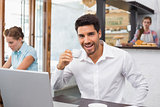 Cheerful man drinking coffee while using laptop in coffee shop