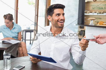 Man receiving coffee while using digital tablet in coffee shop