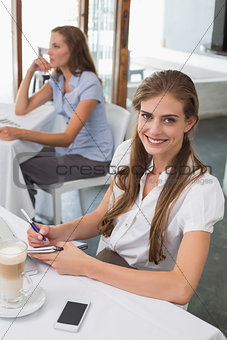 Woman writing notes with laptop in coffee shop