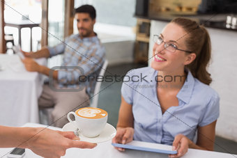 Woman receiving coffee while using digital tablet in coffee shop