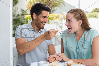Happy man feeding woman at coffee shop