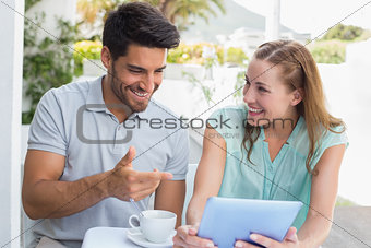 Happy couple with coffee cup using digital tablet at café
