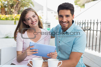 Smiling couple using digital tablet at café