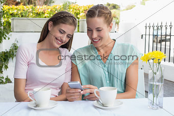 Female friends reading text message at coffee shop