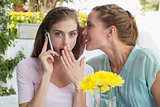 Woman whispering secret into friends ear while shes on call