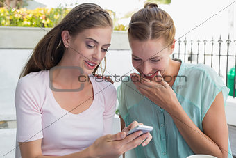 Happy female friends reading text message at coffee shop