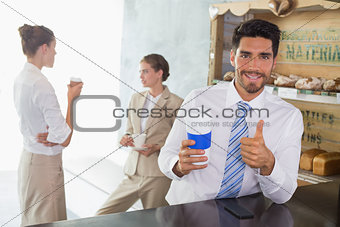 Businessman with coffee sipper gesturing thumbs up in office cafeteria