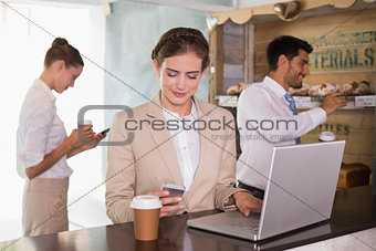 Businesswoman using mobile phone and laptop in office cafeteria