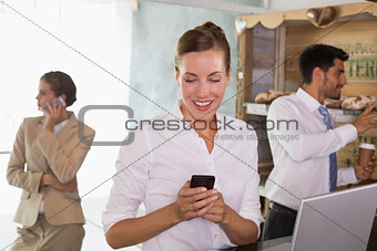 Businesswoman using mobile phone and laptop in office cafeteria