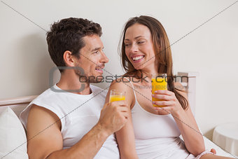 Happy relaxed couple with orange juices in bed