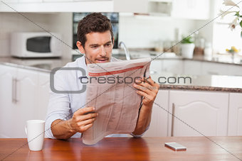 Concentrated man reading newspaper in kitchen