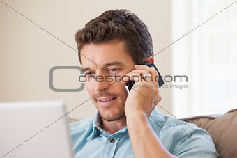 Smiling man using laptop and mobile phone in living room