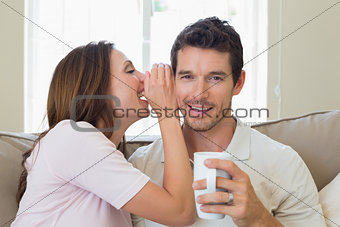 Woman whispering secret into a happy mans ear in living room