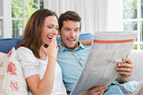 Happy couple reading newspaper on couch