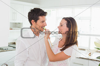 Loving woman feeding man cucumber slice in kitchen