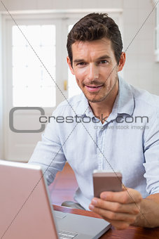 Smiling young man using laptop and mobile phone