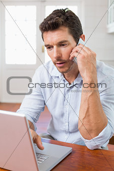 Concentrated man using laptop and mobile phone