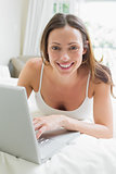 Smiling relaxed woman using laptop in bed