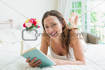 Relaxed smiling woman reading a book in bed