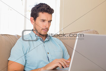 Concentrated young man using laptop on couch