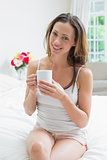 Smiling relaxed woman with coffee cup sitting in bed