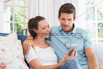 Smiling couple text messaging in living room