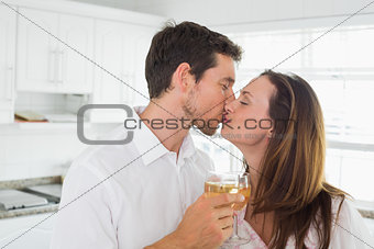 Loving couple kissing with wine glass in hand in kitchen