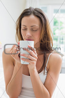Relaxed woman with coffee cup sitting in bed